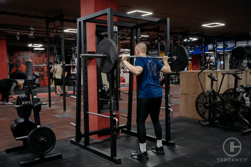 athlete lifts barbell by squat rack