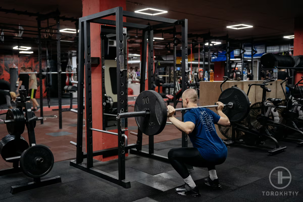 athlete lifts barbell by squat rack
