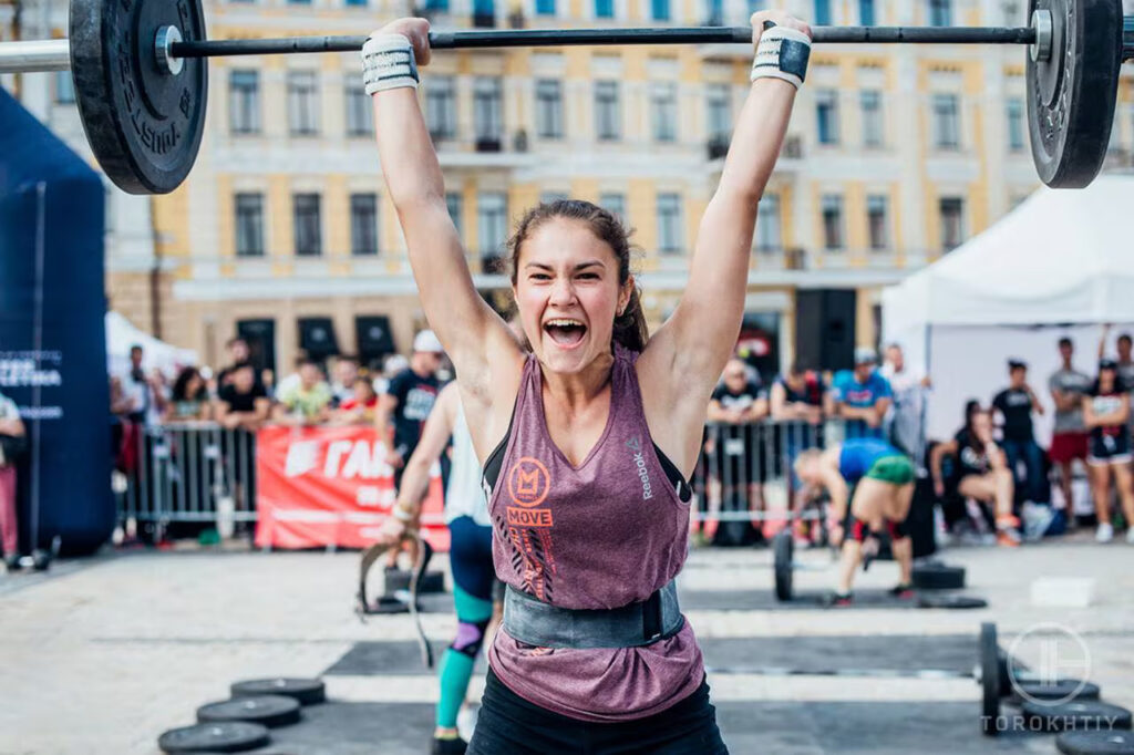 happy athlete woman wearing weight belt and holding barbell