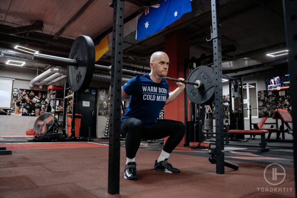 athlete lifts barbell by squat stand in gym