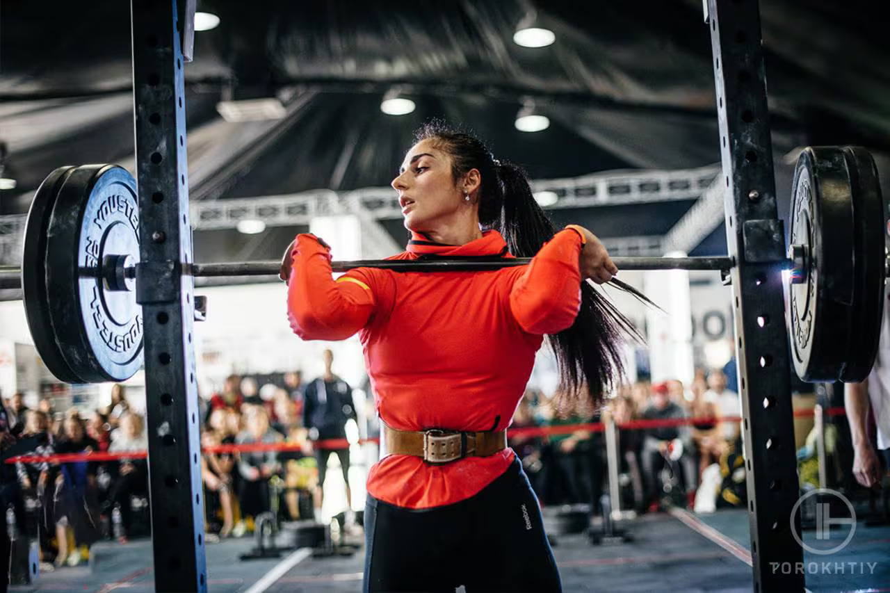 athlete woman wearing weight belt and lifting barbell