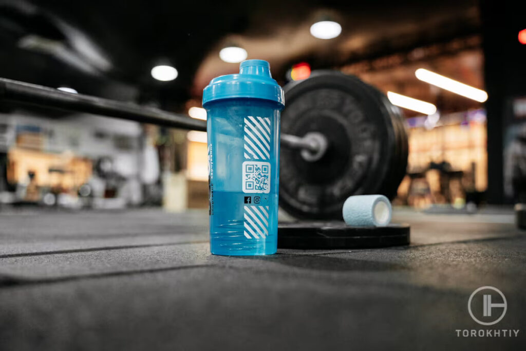 protein supplement shake bottle and barbell in gym